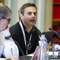 A judge sitting at a table asks a question of the presenting groups, who are out of shot